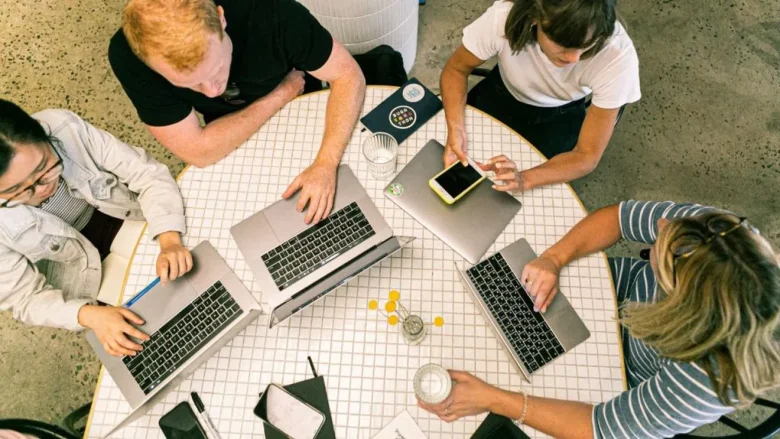 Tineri bărbați și femei lucrând la laptopuri într-un spațiu de coworking. Foto ilustrativ.