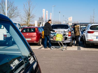 Clienți Kaufland care încarcă cumpărăturile în mașină într-o parcare aglomerată de supermarket